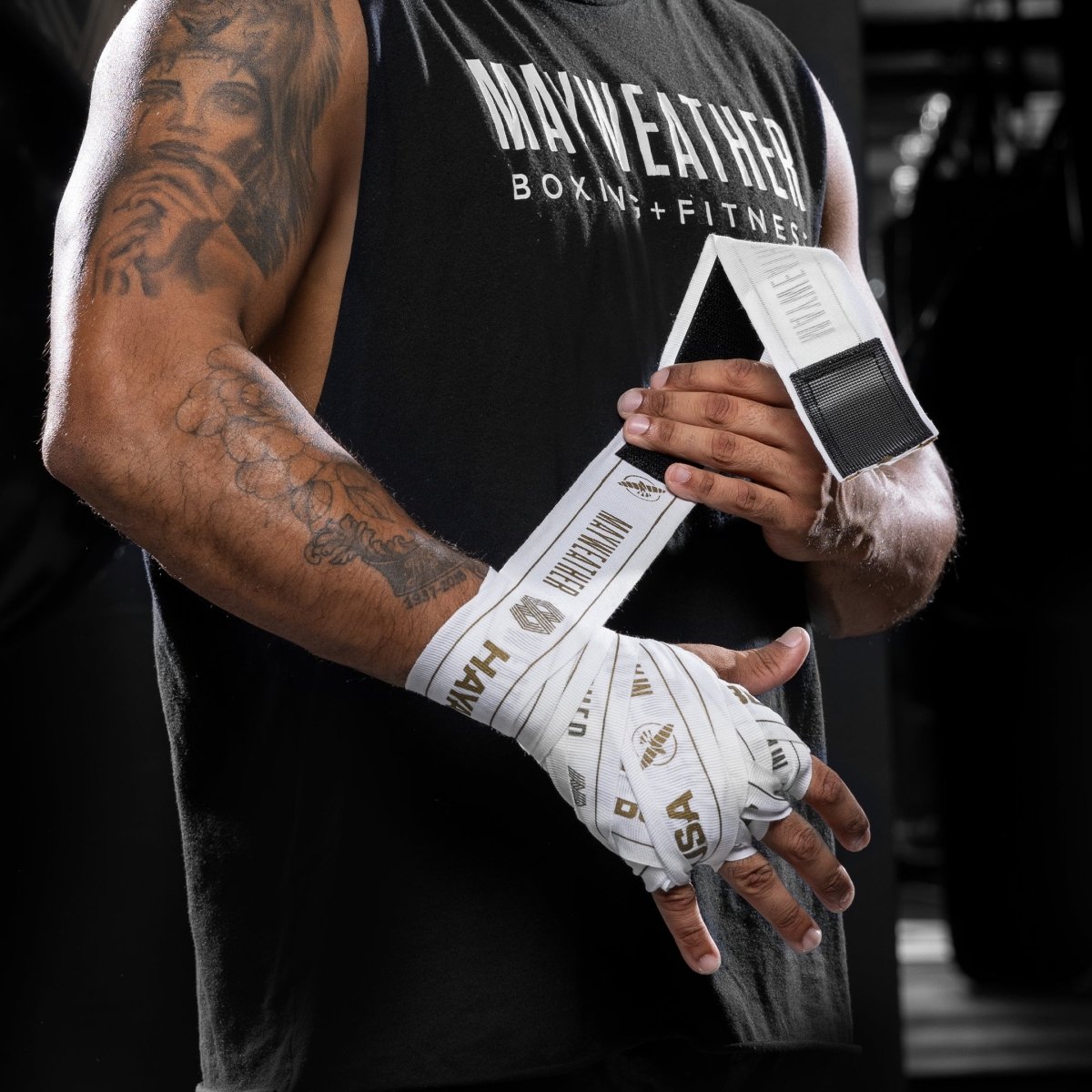 Framifrån av en fighters hand med ett helt bandage med Mayweather Hayabusa 180 tums vitt och guld stretchbandage, med "MAYWEATHER"-logotypen synlig på handledsområdet