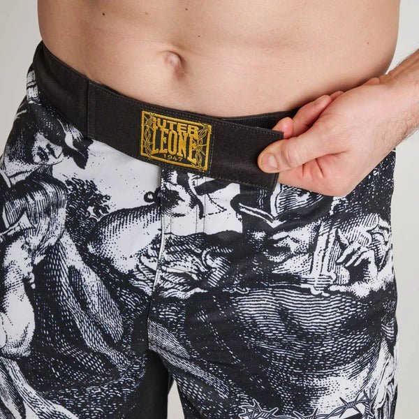Close-up van het voorste sluitpaneel van de LEONE x IUTER short, met het interne trekkoord en de gouddraadpatch op de tailleband
