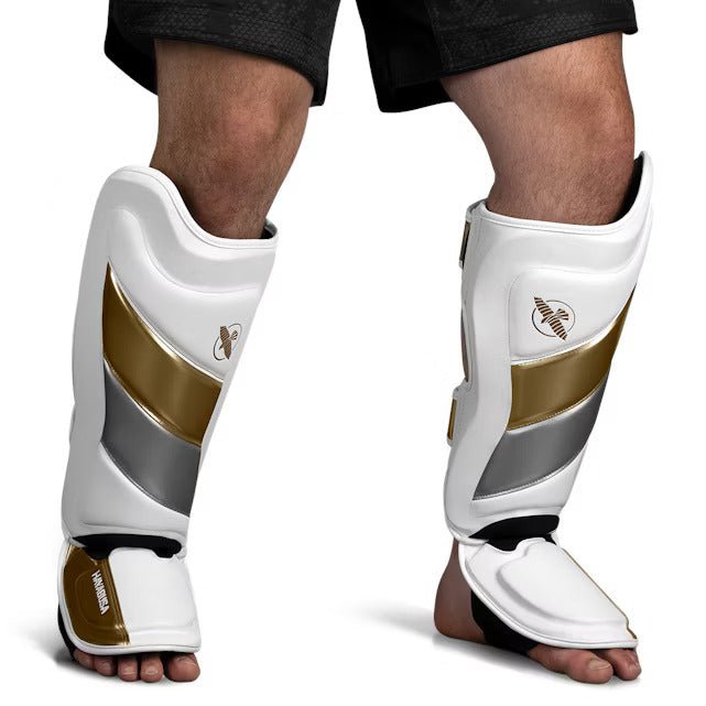 Vue de face du protège-tibia Hayabusa T3 Striking blanc et doré, montrant le rembourrage pré-incurvé