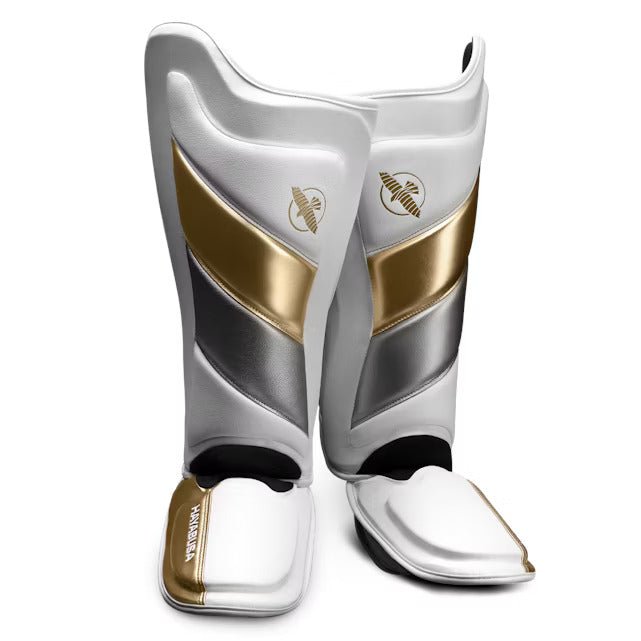 Paire de protège-tibias Hayabusa T3 Striking blancs et dorés pour kickboxing et MMA, vue de face