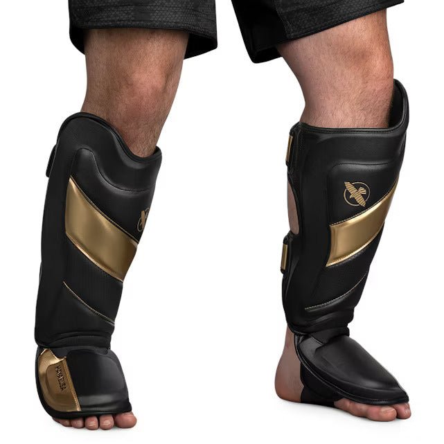 Vue de face du protège-tibia Hayabusa T3 Striking noir et doré, montrant le rembourrage pré-incurvé