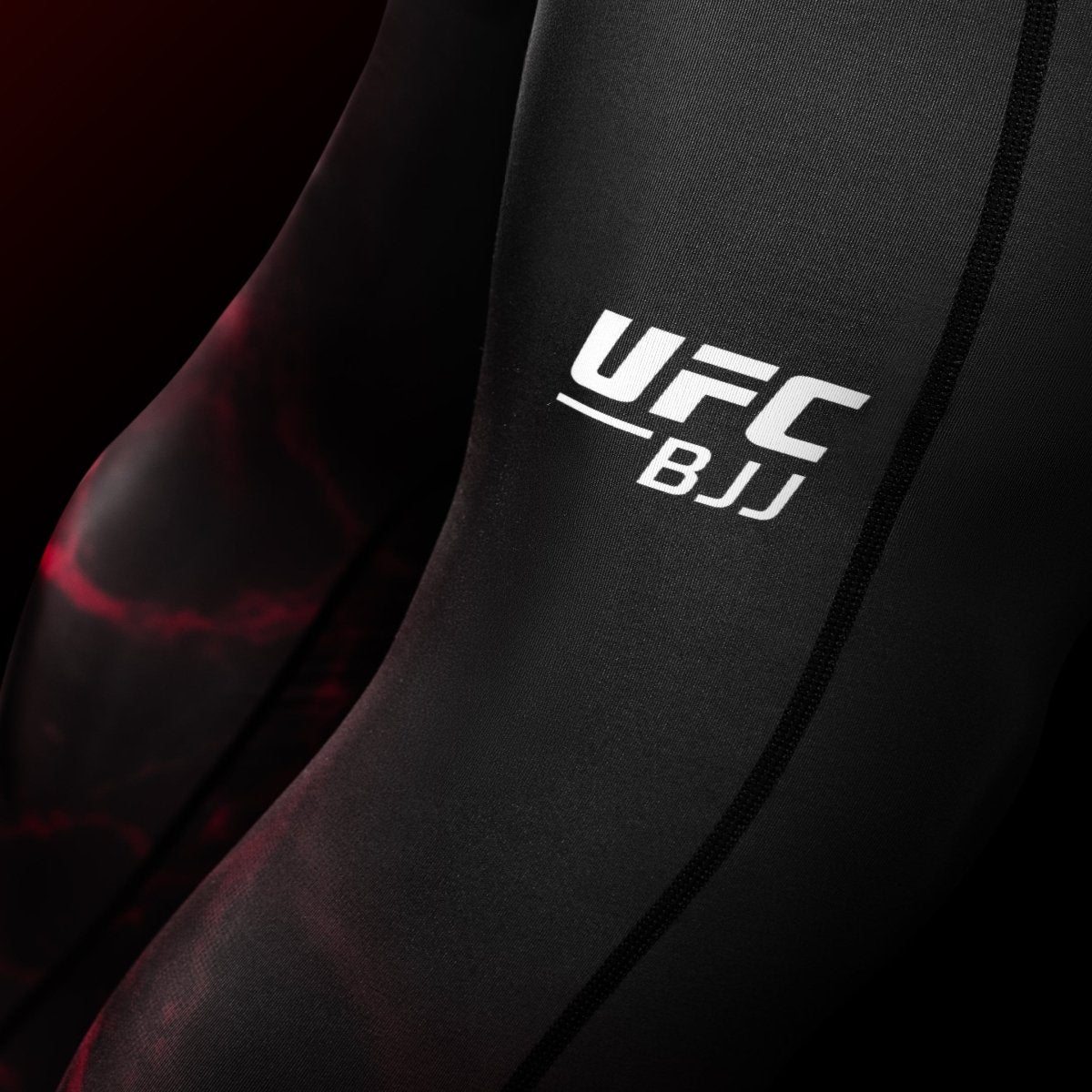 Close da estampa do UFC na perna da legging BJJ Spats preta e vermelha, detalhe da costura reforçada