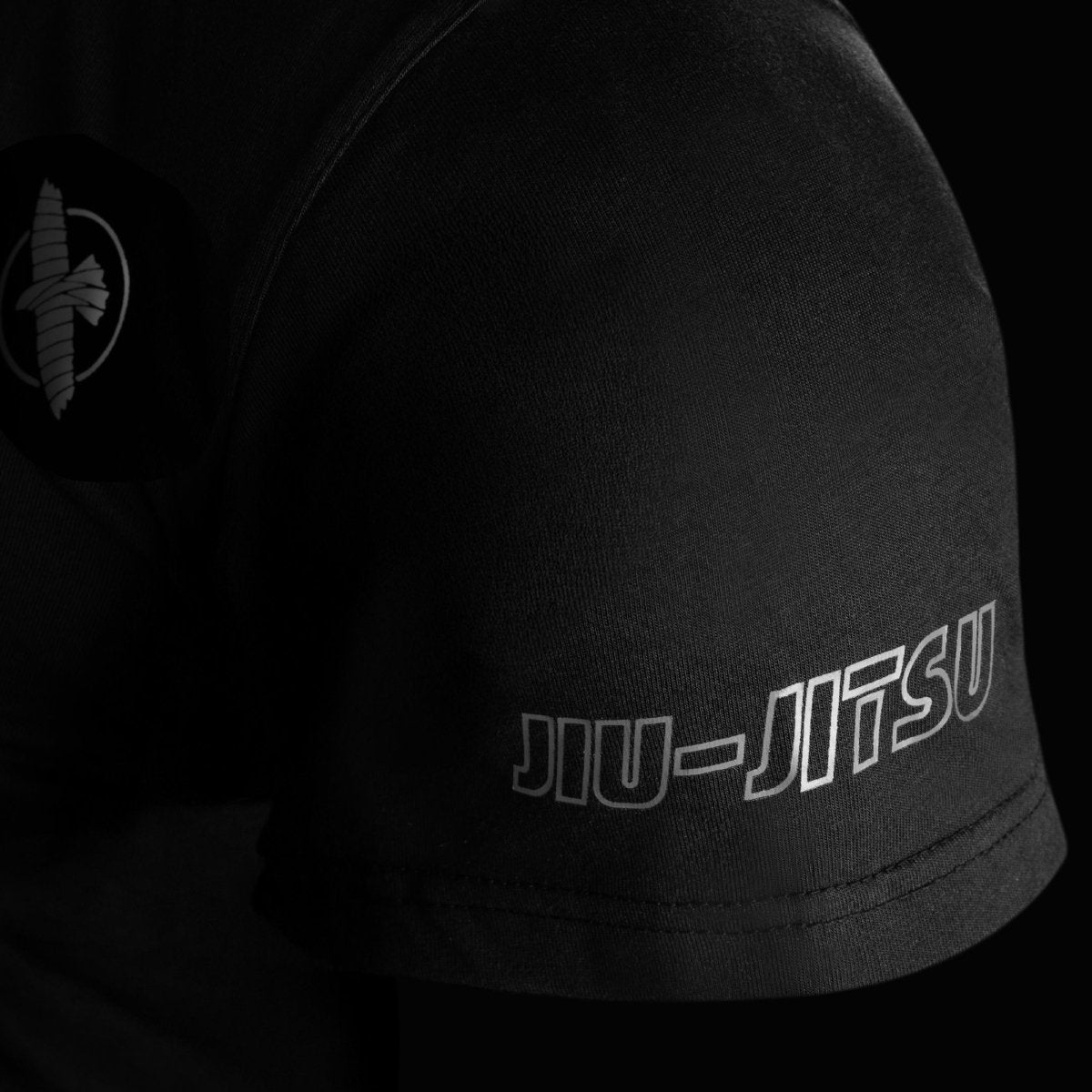 Gros plan sur la manche du t-shirt noir Hayabusa UFC BJJ, montrant les coutures renforcées et le logo faucon brodé